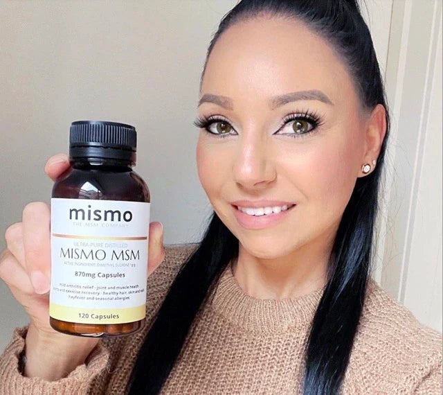 Image of a woman holding a bottle of MISMO MSM capsules, with a label on the bottle reading 'MISMO MSM Capsules'. The woman is holding the bottle with one hand and smiling, appearing happy and satisfied with the product.